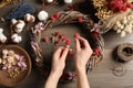 Florist making wreath with dried flowers at wooden table, top view
