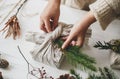 Florist preparing zero waste Christmas gift. Plastic free holidays. Hands decorating stylish christmas gift in linen fabric with