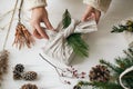 Florist preparing zero waste Christmas gift. Plastic free holidays. Hands decorating stylish christmas gift in linen fabric with