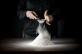 Flour on a kitchen table on a black moody background in the morning light. Woman`s hands sieving flour through a sieve.