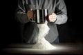 Flour on a kitchen table on a black moody background in the morning light. Woman`s hands sieving flour through a sieve.