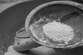 Flour sifting through a metal sieve for a baking. Close up. Black and white