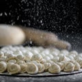 Flouring of uncooked ravioli or dumplings. Cooking process on black background. Close up shot. Soft focus in foreground