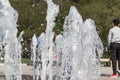 Flow splashes of water of city fountain, foam in jet of water. Fragment of recreation zone of the city park, green trees on