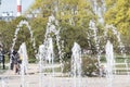 Flow splashes of water of city fountain, foam in jet of water. Fragment of recreation zone of the city park, green trees on