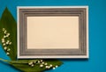 Wooden photo frame and border of spring lilies of the valley Convallaria majalis on a light blue paper background.