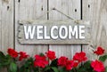 Flower border of red roses by wood welcome sign hanging on distresed wooden fence