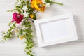 Flower bouquet and a blank white photo frame, copy space, on a white wooden background. Royalty Free Stock Photo