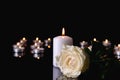 Burning candle and flower on black background