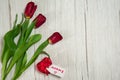 A bouquet of spring tulips in craft paper, a gift box and a note for my mother on a light wooden background. Royalty Free Stock Photo