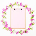 Flower frame of pink flowers and clipboard with pink paper on white background. Flat lay Royalty Free Stock Photo