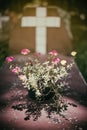 Flower in front of a cross, in a cemetery, with a vintage filter.stone cross on gravestone - christian cross on grave.Headstone in Royalty Free Stock Photo