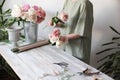 Flower girl at the workplace: flowers, tools and accessories on a light wooden table. Woman florist collects a bouquet of fresh fl Royalty Free Stock Photo