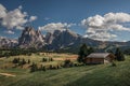 Flower meadows with wooden cabins at Alpe di Siusi during summer with view to mountains of Plattkofel and Langkofel in Dolomites