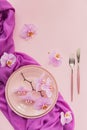 Flower and table settings overhead composition on light pink background. Pink ceramic plates, cutlery and perple orchid flowers.