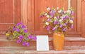 Flower pot with beautiful petunias, empty white frame and clay vase with bellflowers on steps of rustic wooden ladder