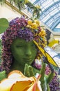 A flower sculpture of a woman with a butterfly in her hand at Bellagio Conservatory and Botanical Gardens with colorful flowers