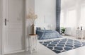 Flower in silver vase on the wooden table next to closed door to elegant new york style bedroom with patterned carpet and white fu