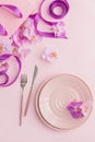 Flower and table settings overhead composition on light pink background. Pink ceramic plates, cutlery, pink gift bag with purple