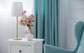 Flower vase and golden table lamp with blue armchair and curtains Royalty Free Stock Photo