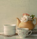 Flower in a yellow tea pot and vintage cup of coffee on wooden b Royalty Free Stock Photo