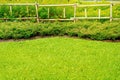 Flowerbeds with green grass in the garden, fence made of bamboo, Garden with a Freshly Mowed Lawn.