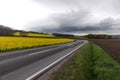 Flowering rapeseed field next to a winding road in the mountains with dramatic clouds Royalty Free Stock Photo