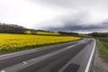 Flowering rapeseed field next to a winding road in the mountains with dramatic clouds Royalty Free Stock Photo