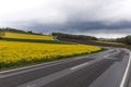 Flowering rapeseed field next to a winding road in the mountains with dramatic clouds Royalty Free Stock Photo