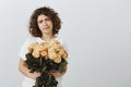 Flowers, again, how boring. Portrait of unimpressed unsatisfied attractive female with curly hair, holding beautiful