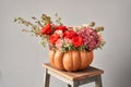 Flowers arrangement in pumpkin on wooden table. Fresh cut flowers for decoration home. European floral shop. Delivery