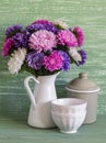 Flowers asters in a white enameled pitcher and vintage crockery - ceramic bowl and enameled jar, on a blue wooden background.