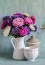 Flowers asters in a white enameled pitcher and vintage crockery - ceramic bowl and enameled jar, on a blue wooden background.