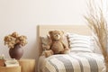 Flowers in brown vase on wooden nightstand table next to single bed with stripped bedding with teddy bear Royalty Free Stock Photo