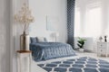 Flowers in gold vase in white bedroom interior with patterned carpet in front of blue bed. Real photo Royalty Free Stock Photo