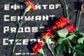 Flowers on the memorial to fallen soldiers, red carnations on black marble, Russian text of soldiers military rank - sergeant,