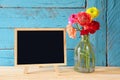 Flowers next to empty blackboard, on wooden table. copy space