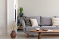 Flowers next to grey couch with pillows in minimal living room interior with wooden table Royalty Free Stock Photo