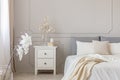 Flowers on nightstand table in delightful bedroom interior with grey and white design