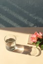 Flowers, notes, glass of water on beige table with shadow