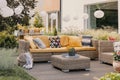 Flowers on rattan table near couch with patterned cushions on the terrace with lanterns.