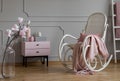 Flowers and rocking chair with blanket in grey and pink living room interior with cabinet. Real photo