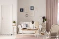 Flowers on table in front of white sofa in pink living room interior with door and armchair. Real photo Royalty Free Stock Photo