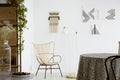 Flowers on table near modern armchair in bright apartment interior with lamp and posters. Real photo