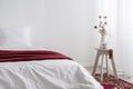 Flowers on table next to white bed with red blanket in minimal bedroom interior