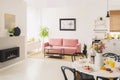Flowers at table in white apartment interior with poster above pink settee near fireplace. Real photo Royalty Free Stock Photo