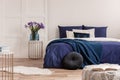 Flowers in vase on bedside table next to king size bed with navy blue bedding Royalty Free Stock Photo
