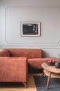 Flowers in vase and red fruits in bowl on wooden coffee table in elegant living room interior with ginger sofa