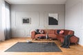 Flowers in vase and red fruits in bowl on wooden coffee table in elegant living room with ginger sofa