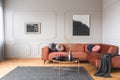 Flowers in vase and red fruits in bowl on wooden coffee table in elegant living room interior with ginger sofa